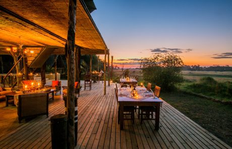 Holzdeck mit gedeckten Tischen u. Sonnenuntergang @ The Hide safari camp