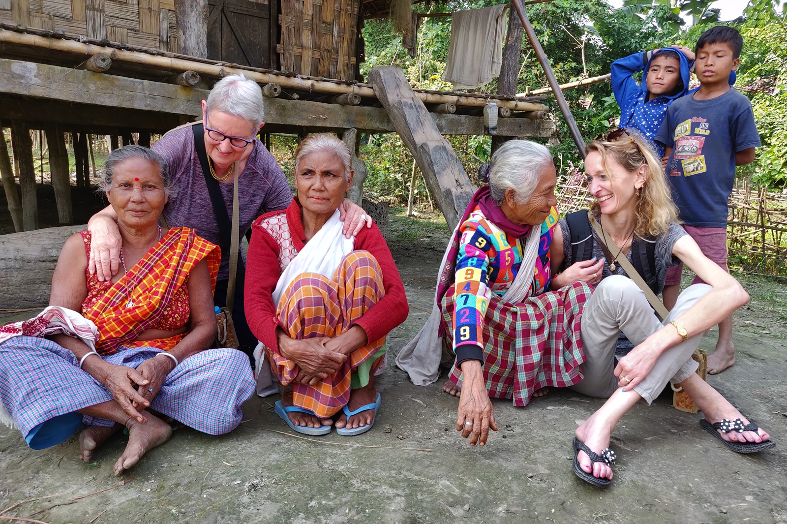 Besucherin sitzt am Boden zusammen mit Bewohnern eines Mishing Dorfes in Indien