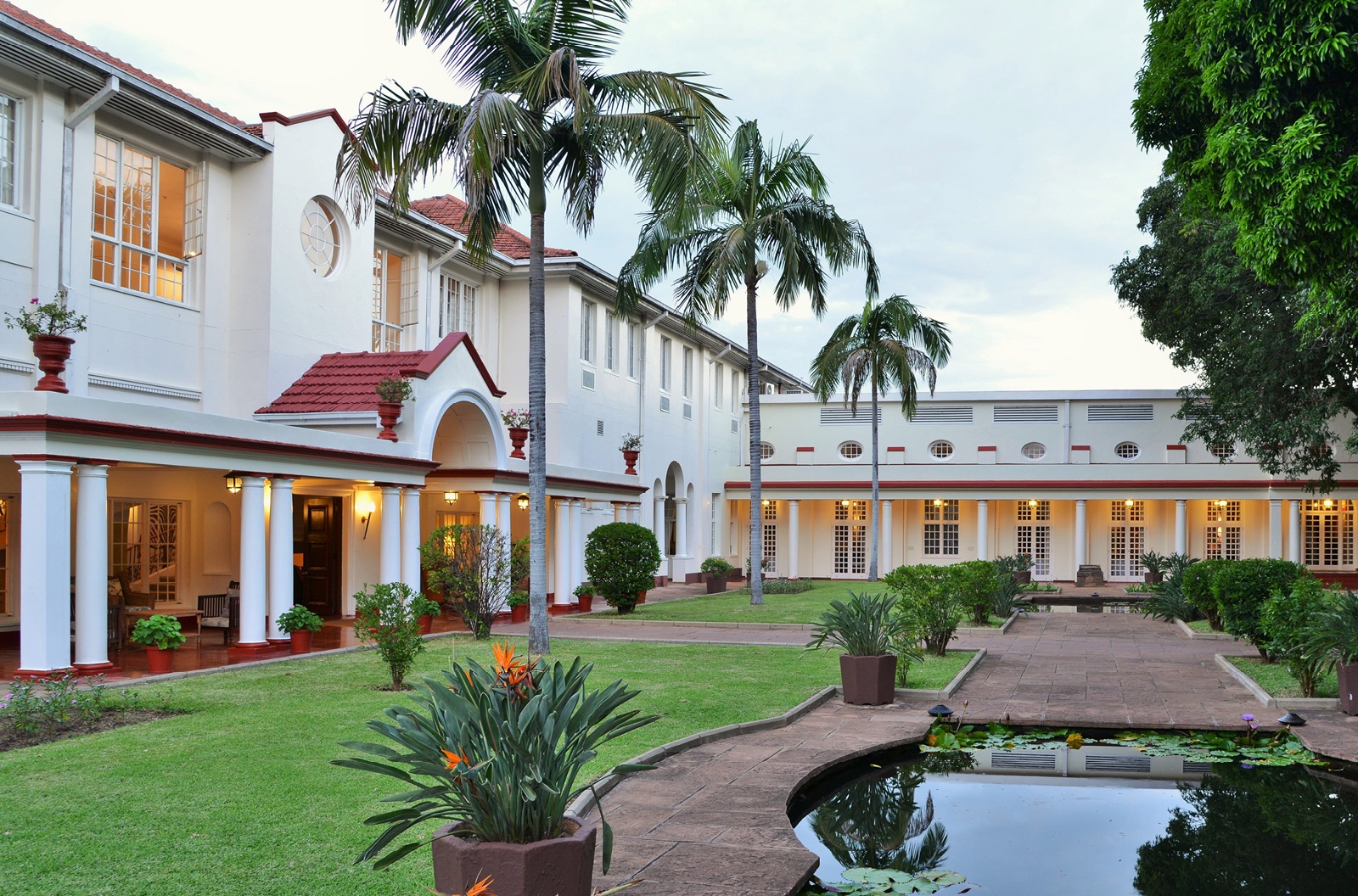 Garten mit Rasen & Palmen sowie Teilansicht der weißen Victoria Falls River Lodge.