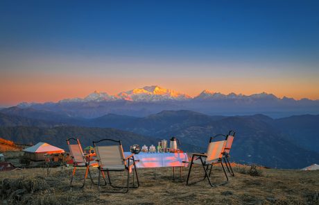 mit Kaffee gedeckter Campingtisch & Stühlen im Freien mit Blick auf golden gefärbten Himalaya