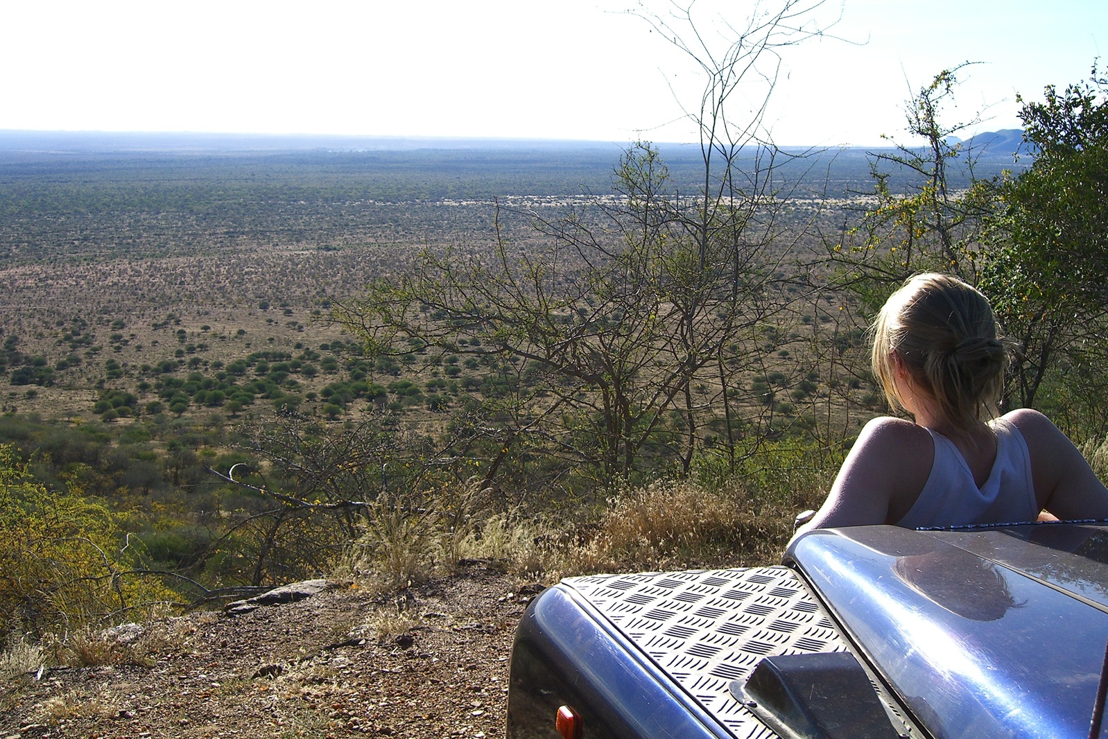 Frau lehnt am Kühler eines Landrovers u. blickt in die Ferne