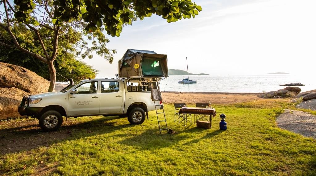 Toyota Hilux mit Dachzelt, Campinghtisch u. Stuhl am Seeufer